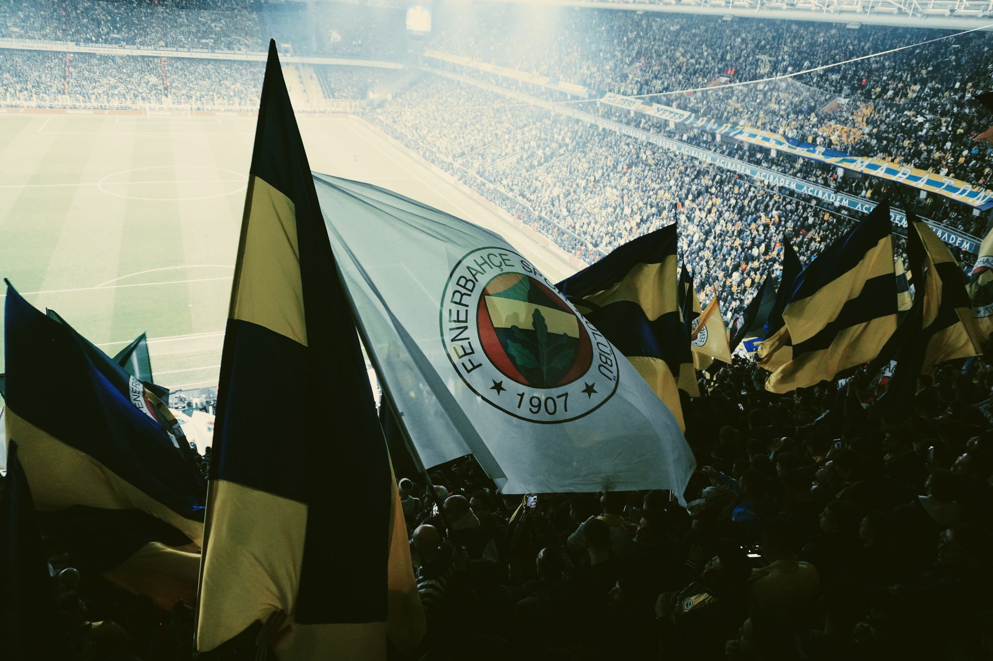 Aficionados de fútbol en las gradas de un estadio de noche, con banderas y bufandas