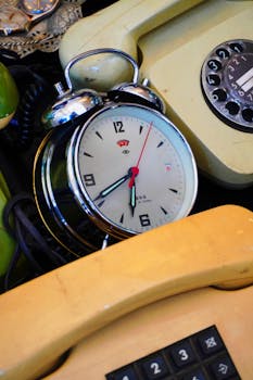 Close-up of a vintage alarm clock surrounded by retro rotary and push-button telephones.