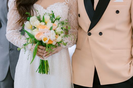 Bride and groom standing together holding a vibrant floral bouquet, showcasing elegance and romance.