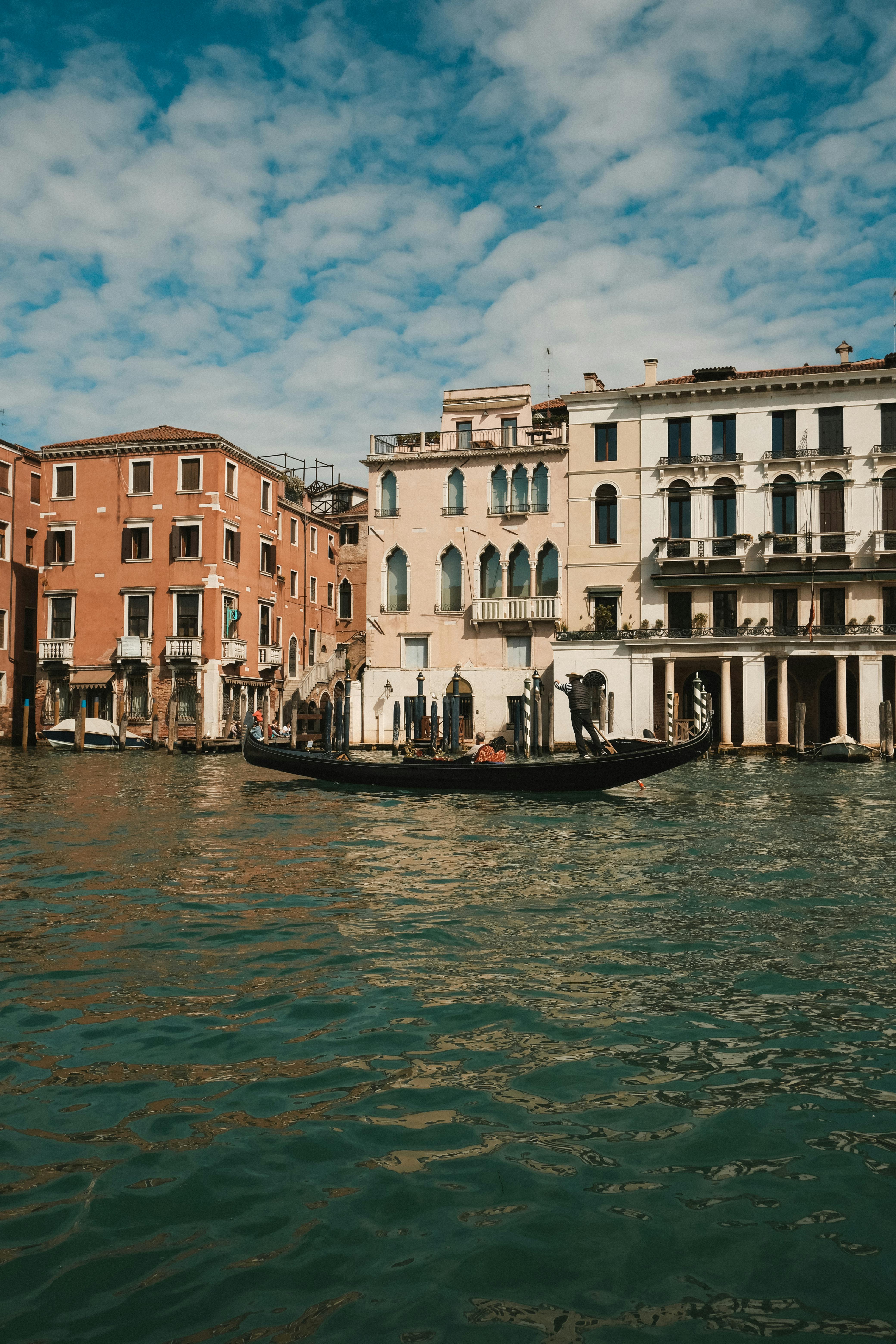 Gondola gliding on a Venetian canal, surrounded by historic colorful buildings under a bright sky.