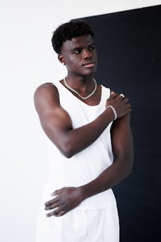 Confident young man in white tank top posing against black background.