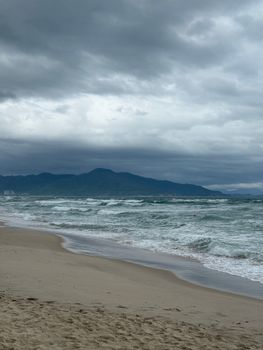 Scenic view of a cloudy beach with mountainous backdrop and rolling waves.