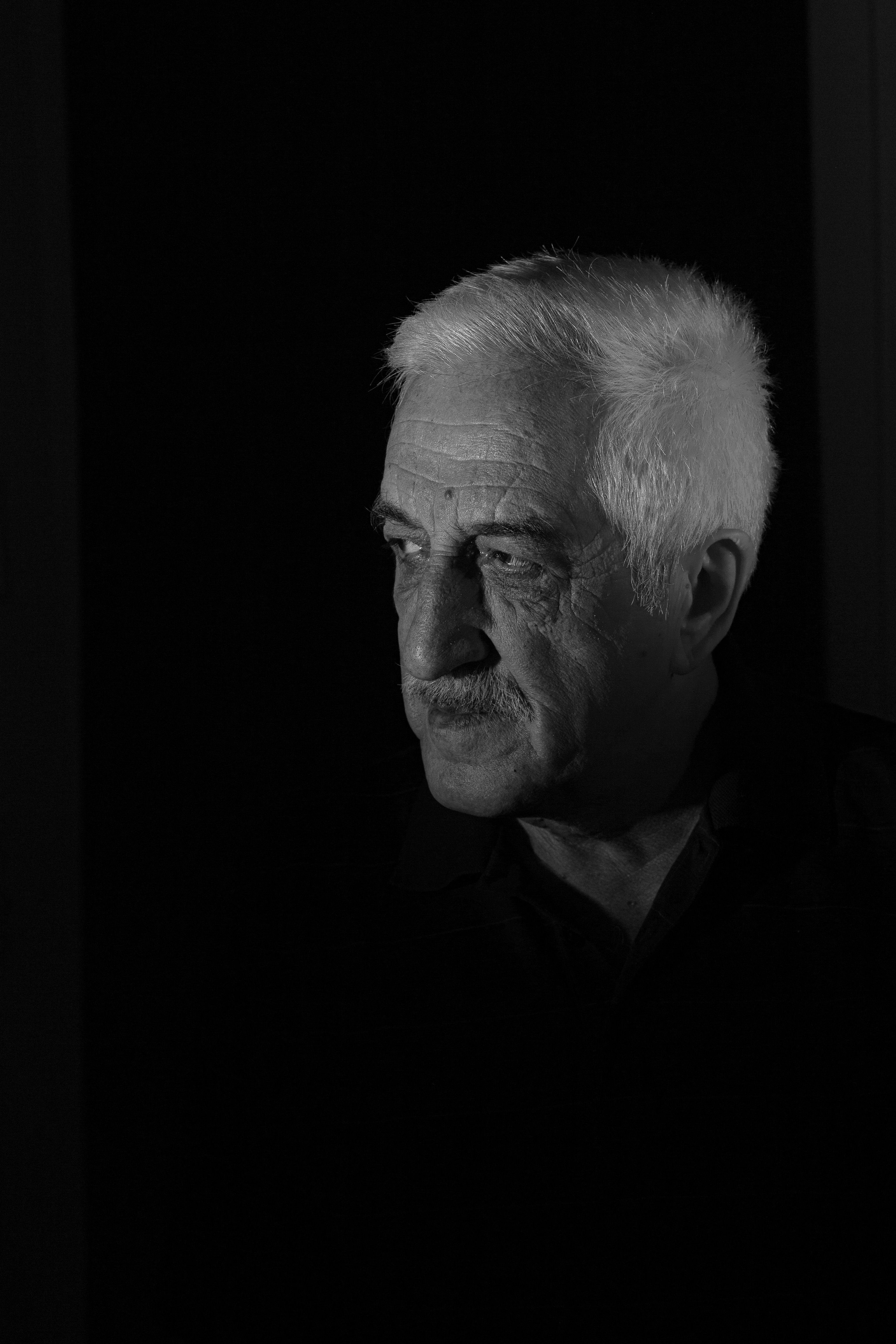 Black and white portrait of a senior man looking contemplative in dramatic lighting.