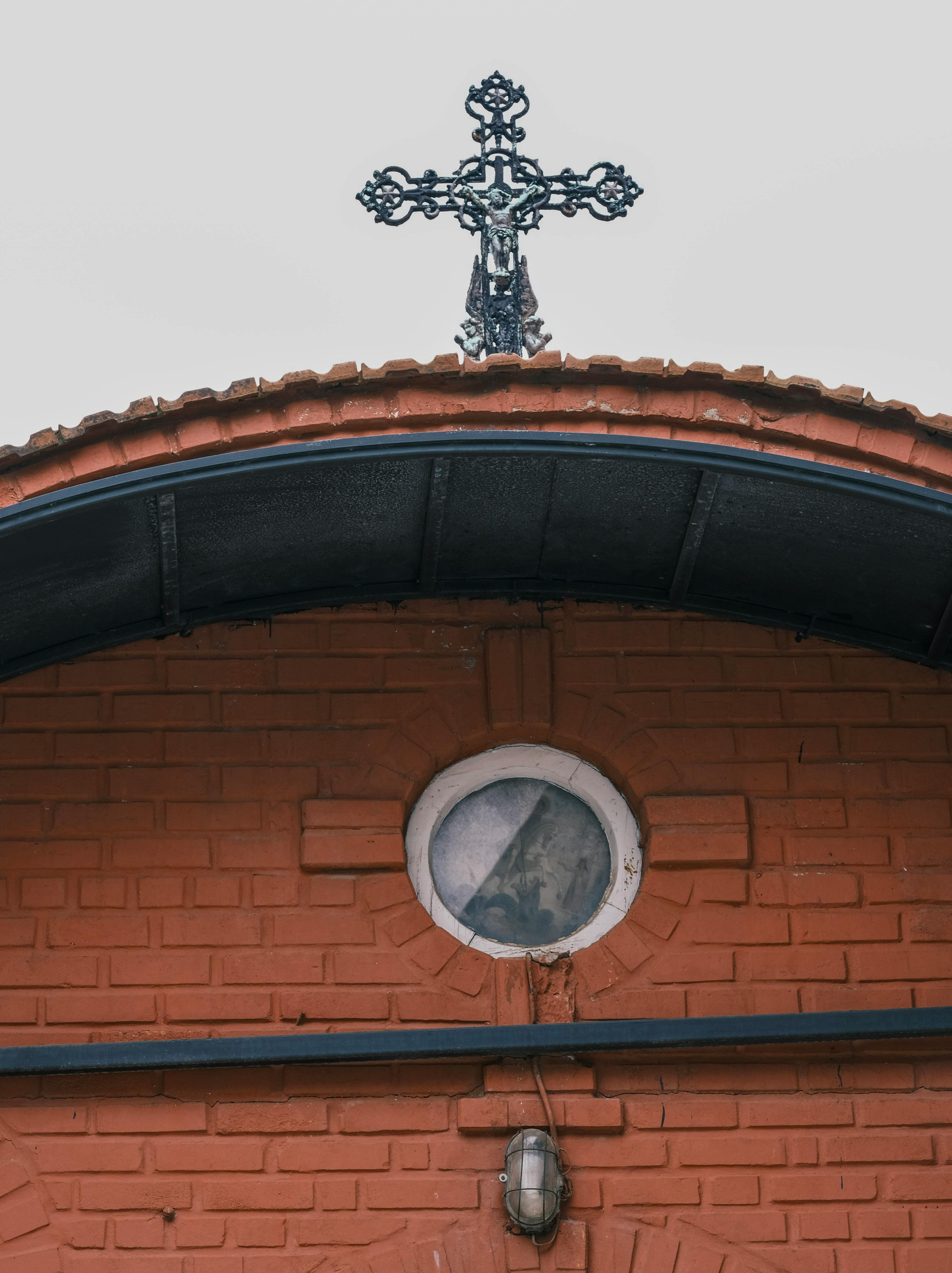 Close-up of a brick church facade featuring an ornate iron cross and circular window.