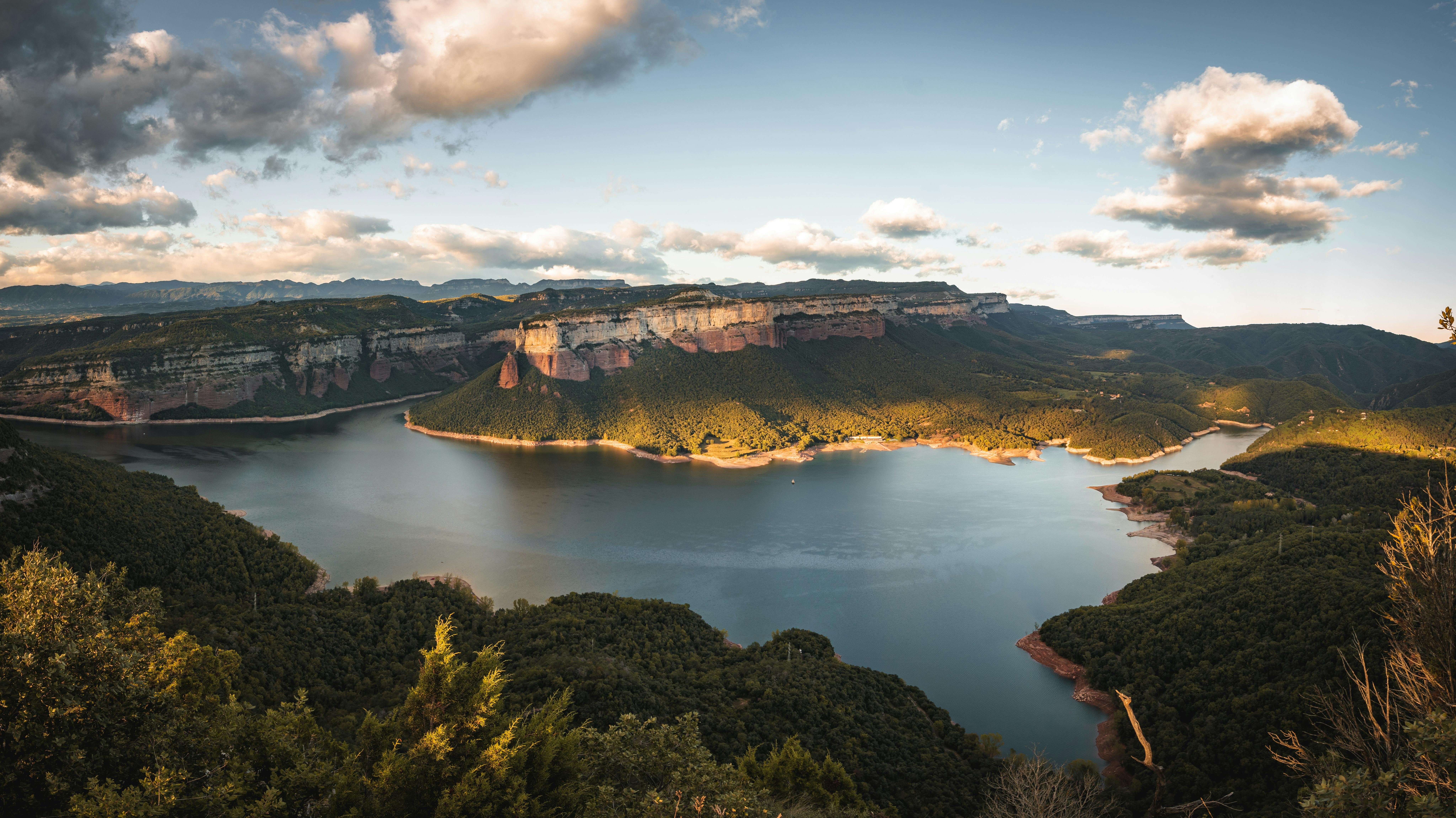 A breathtaking aerial view of a dam in a mountainous landscape under a partly cloudy sky.