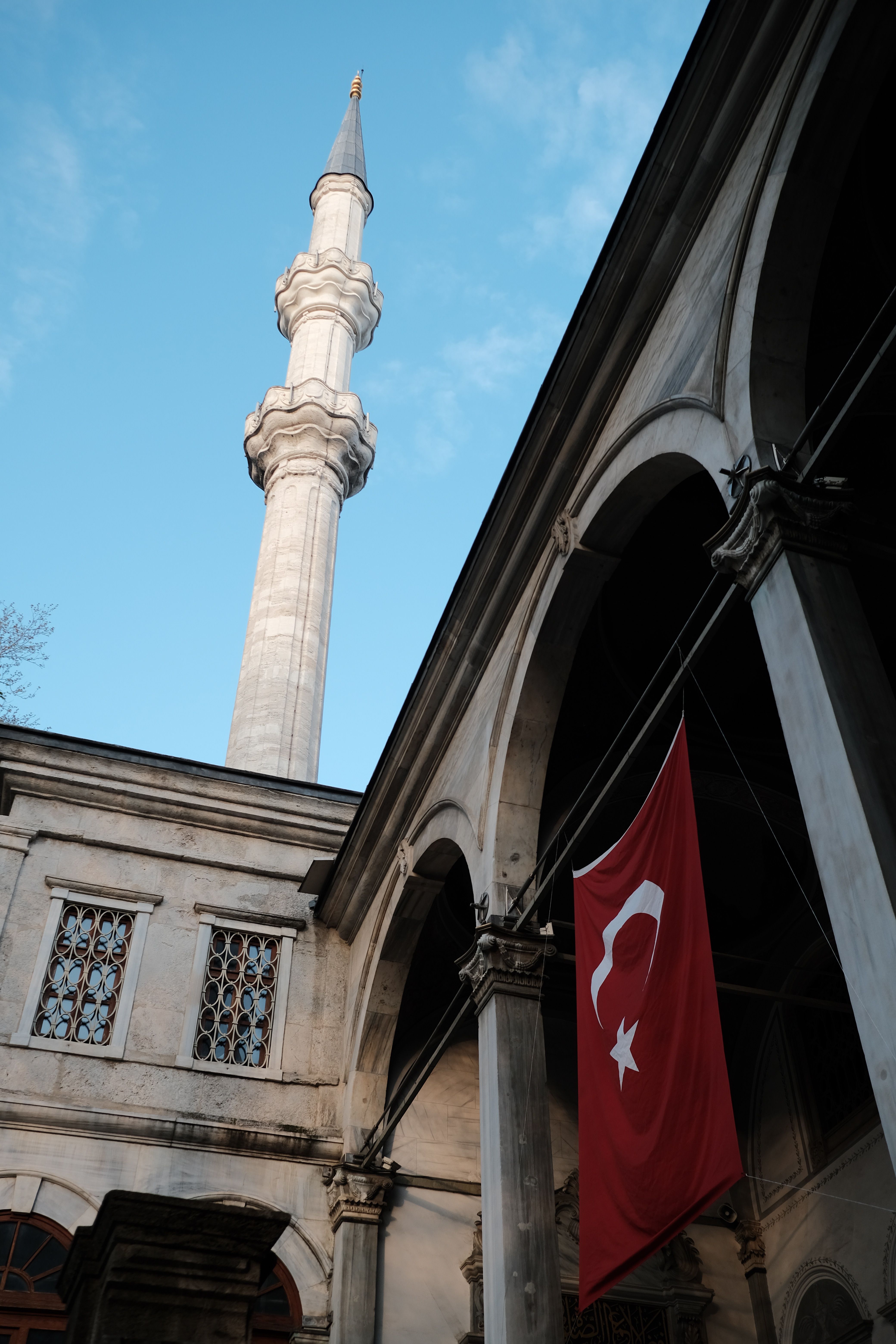 Beautiful view of a mosque minaret and Turkish flag in Istanbul, Türkiye, under a clear blue sky.