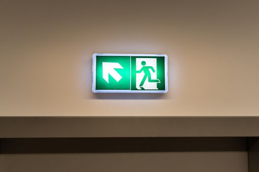 Bright green emergency exit sign with arrow symbol in indoor hallway, indicating direction to safety.