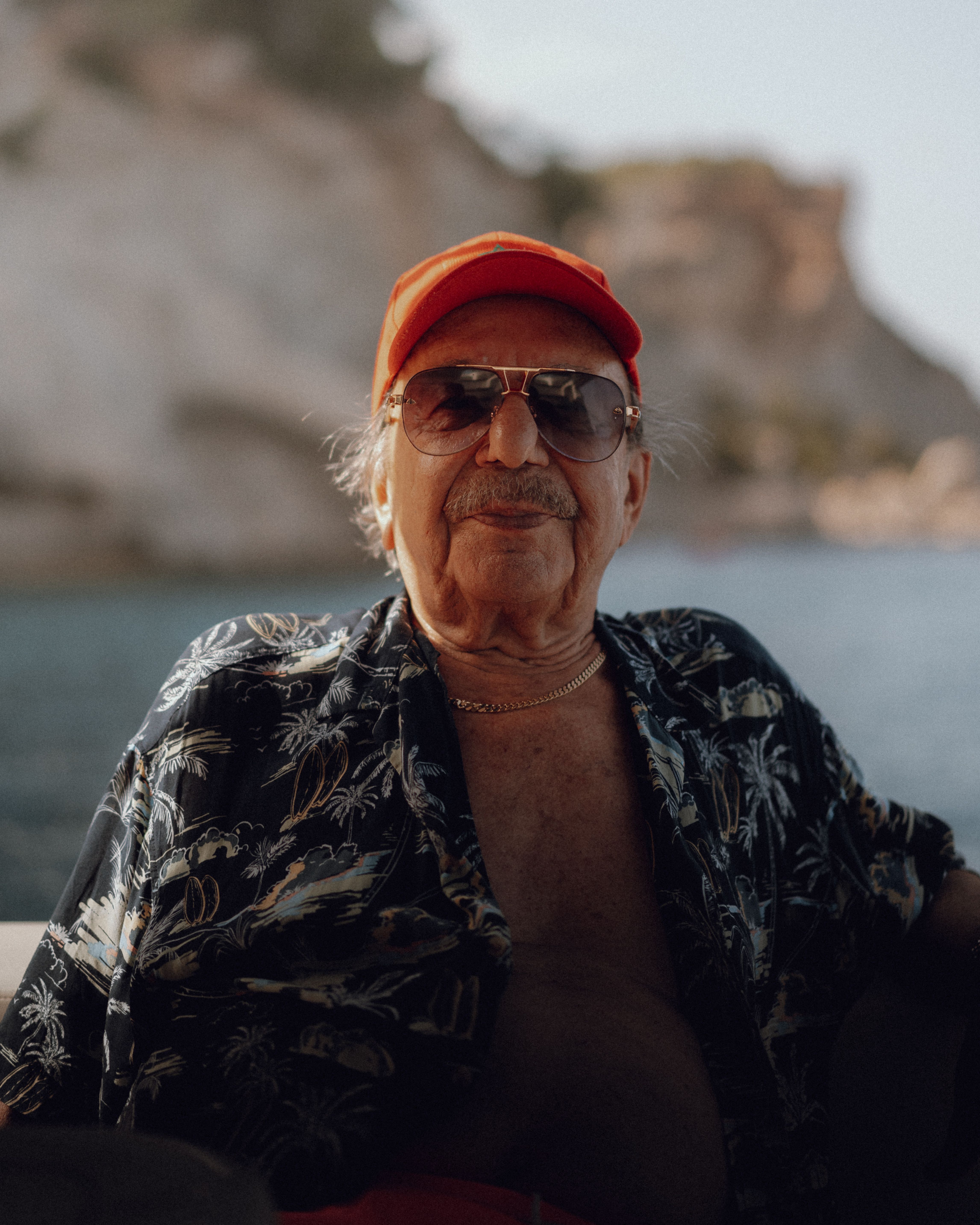 Elderly man in a floral shirt and cap, enjoying a scenic outdoor summer view.