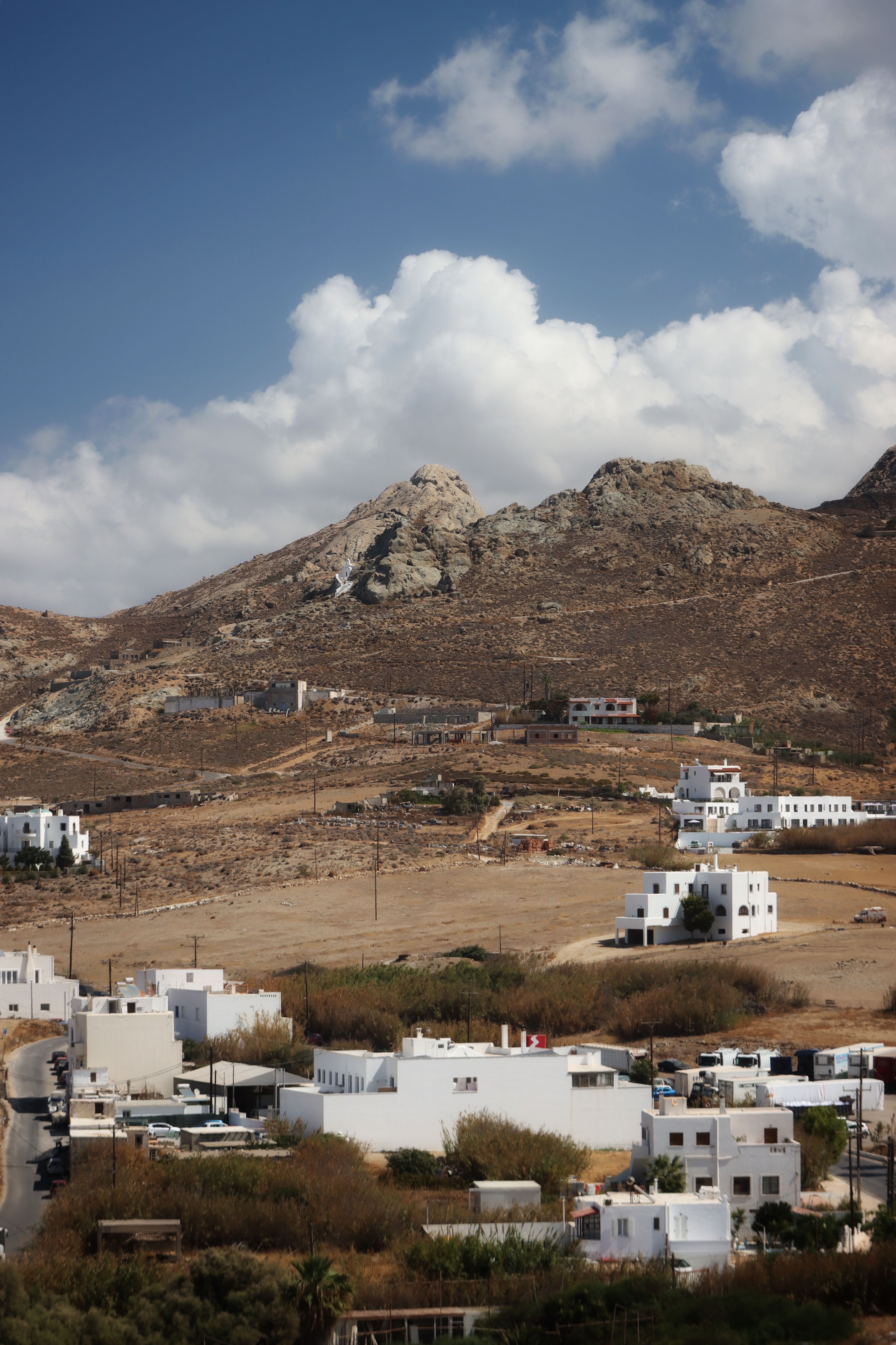 A picturesque view of white houses and rocky hills under a bright blue sky in Naxos, Greece.
