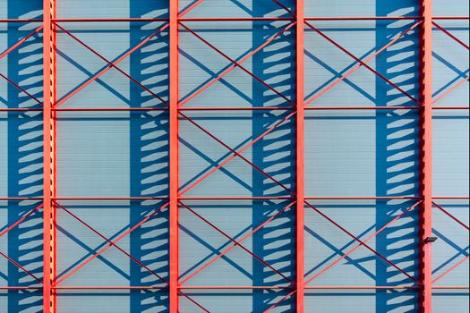 Abstract photo featuring a red metal framework casting blue shadows on a wall.