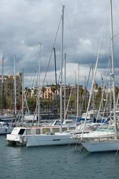 Sailing boats docked at Port Vell, Barcelona, under a cloudy sky, showcasing maritime charm.
