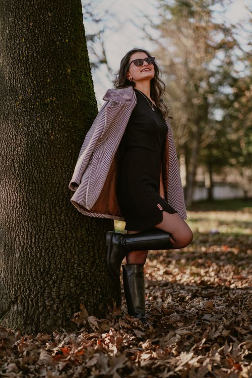 Free Fashionable woman in fall outfit leaning against a tree outdoors. Stock Photo