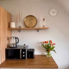 Bright kitchen corner with a small black two-slice toaster beside a microwave on a wooden worktop, tulips in a vase and a shelf above