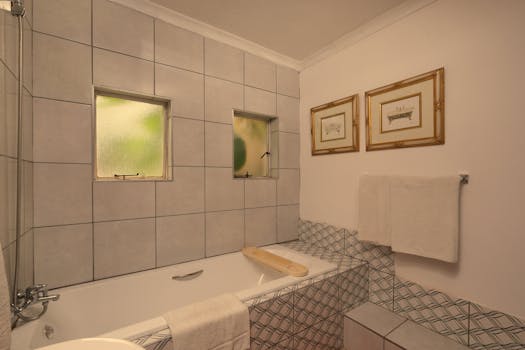 A cozy bathroom featuring a white bathtub, patterned tiles, and framed wall art.