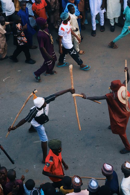 Free Overhead view of a vibrant street parade with participants engaging in a traditional stick fight performance. Stock Photo