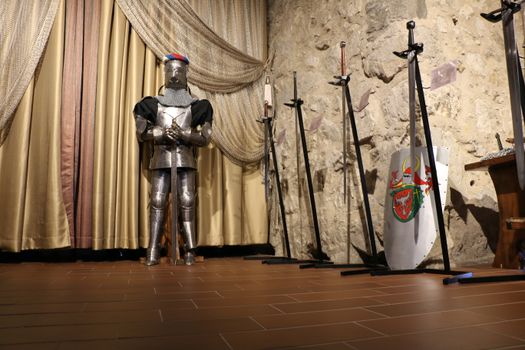 A knight's armor and swords displayed in a historic room with stone walls.
