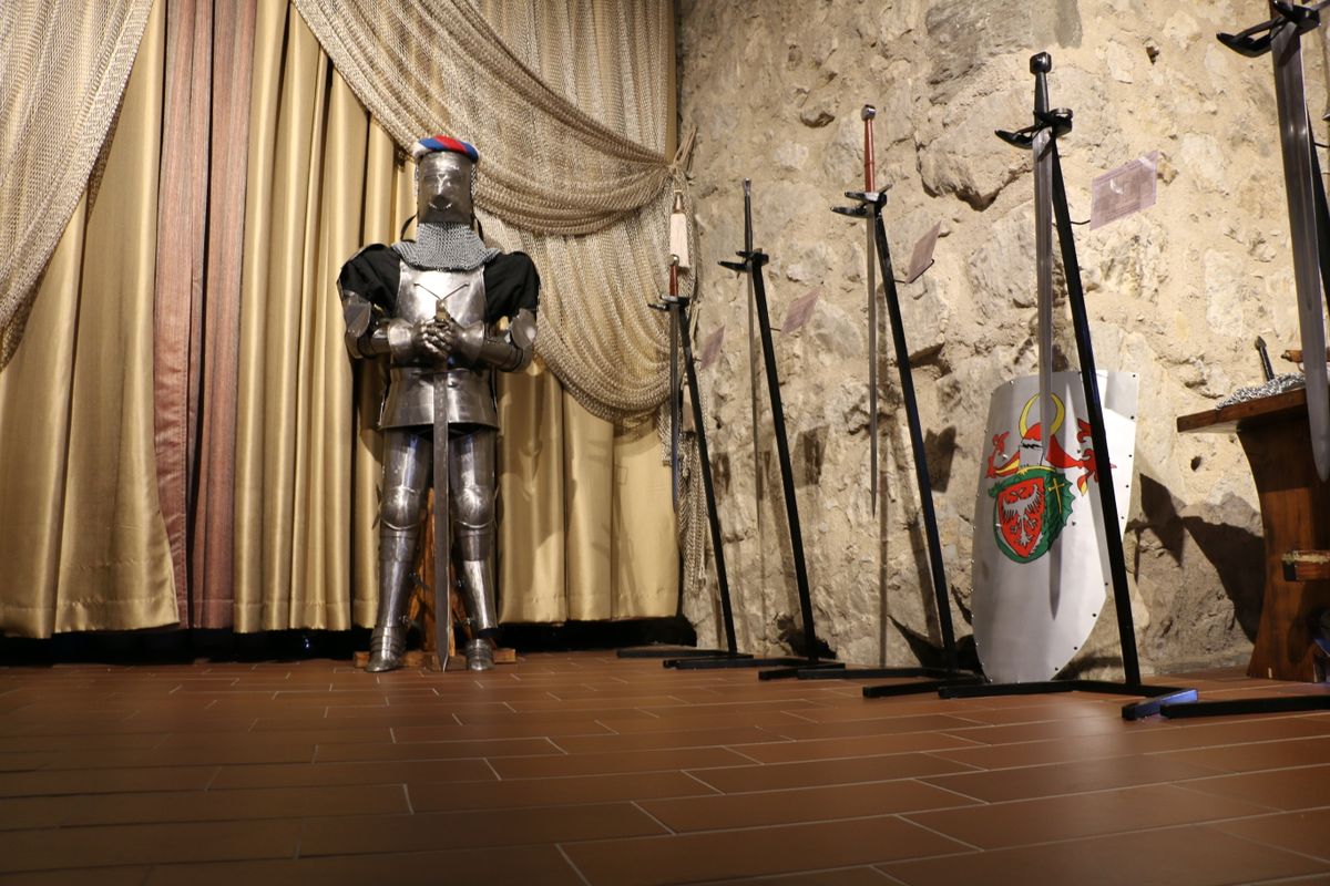 A knight’s armor and swords displayed in a historic room with stone walls.