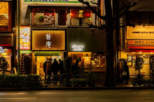 A bustling street in Tokyo with illuminated ramen shops and patrons at night.