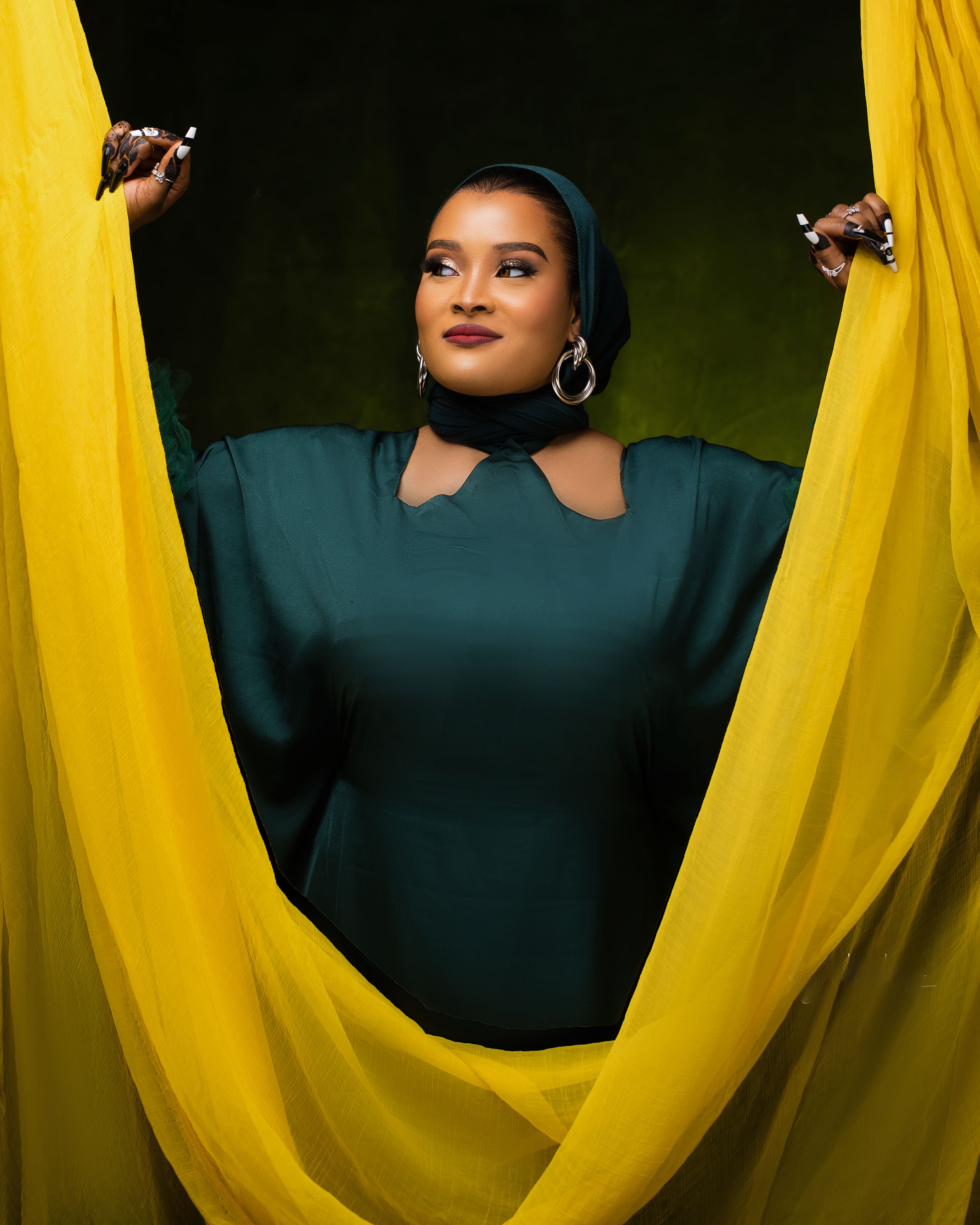 Portrait of a confident woman wearing traditional attire, framed by vibrant yellow drapes.