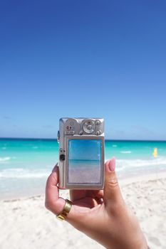 Close-up of a camera held at a beach capturing the ocean and sky.