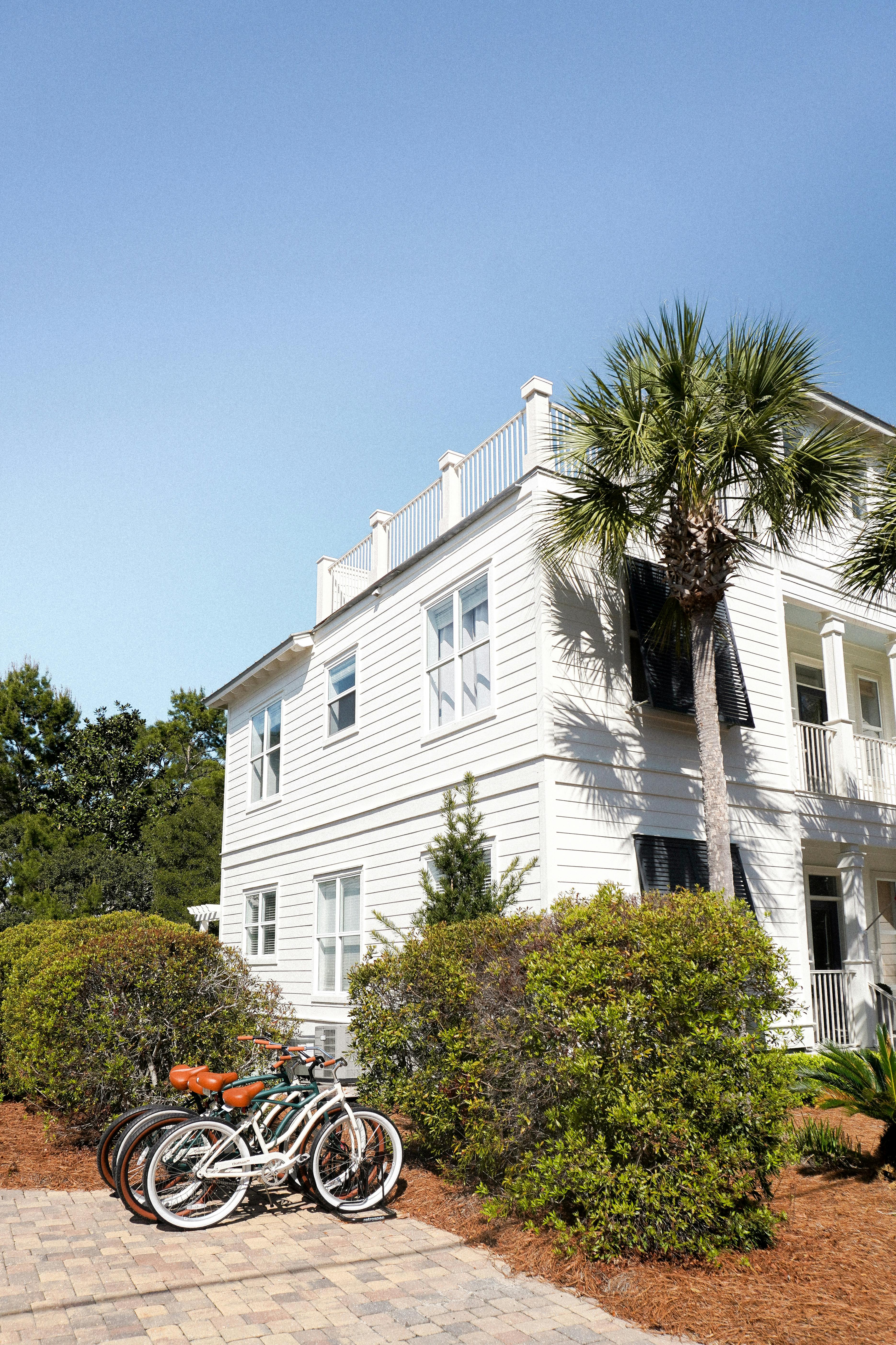 Free White coastal house with bicycles and palm tree under blue sky, perfect for real estate and travel imagery. Stock Photo