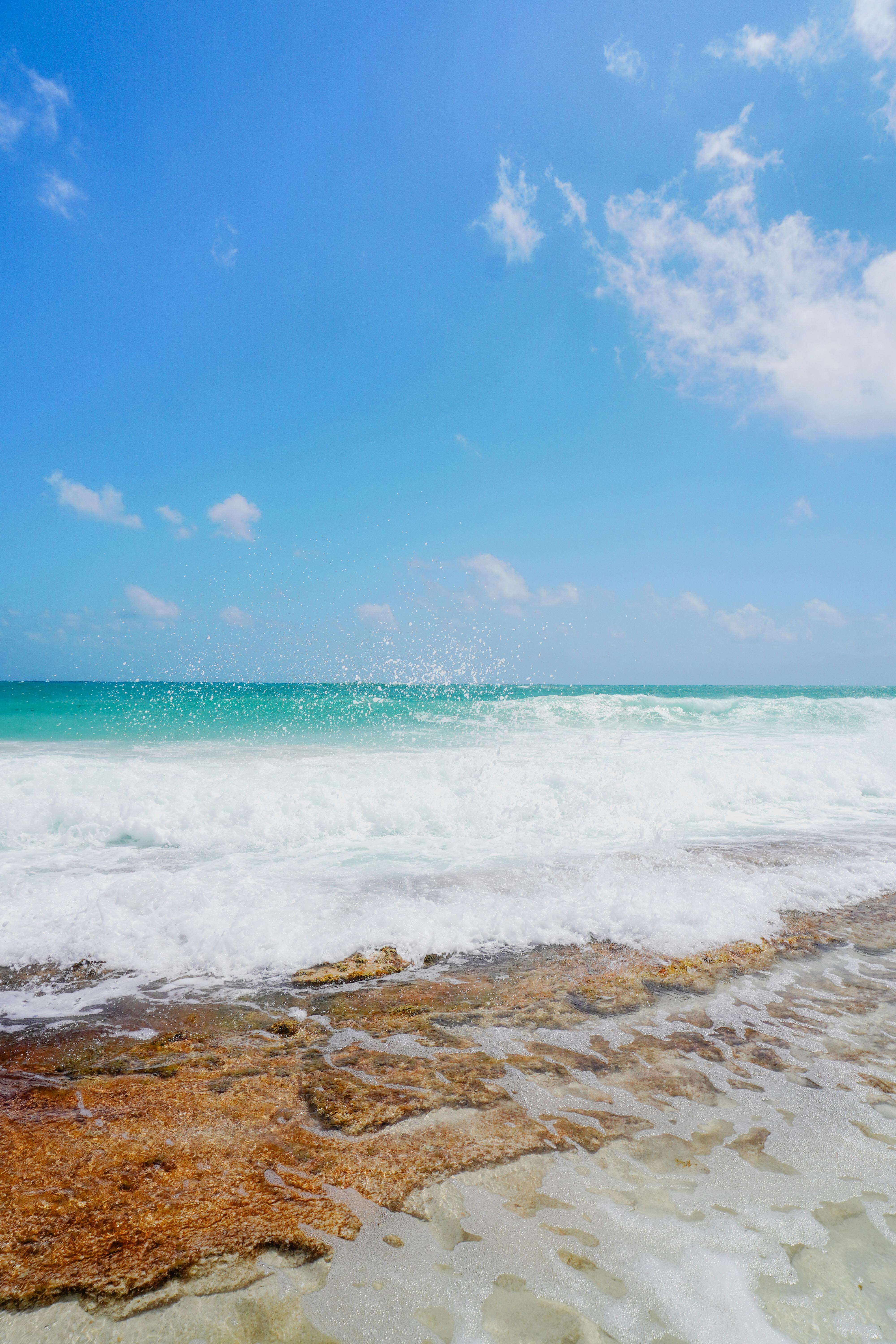 Vibrant beach scene with turquoise waves crashing against rocks under a clear blue sky.