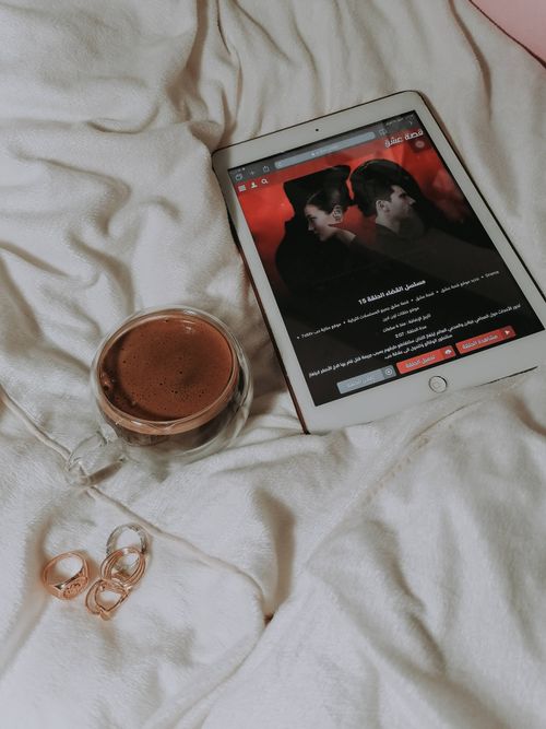 Free Relaxing setup with a tablet, hot drink, and jewelry on soft bedding. Stock Photo