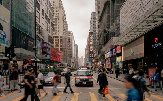 Dynamic view of a busy Hong Kong street with pedestrians and taxis during the day.