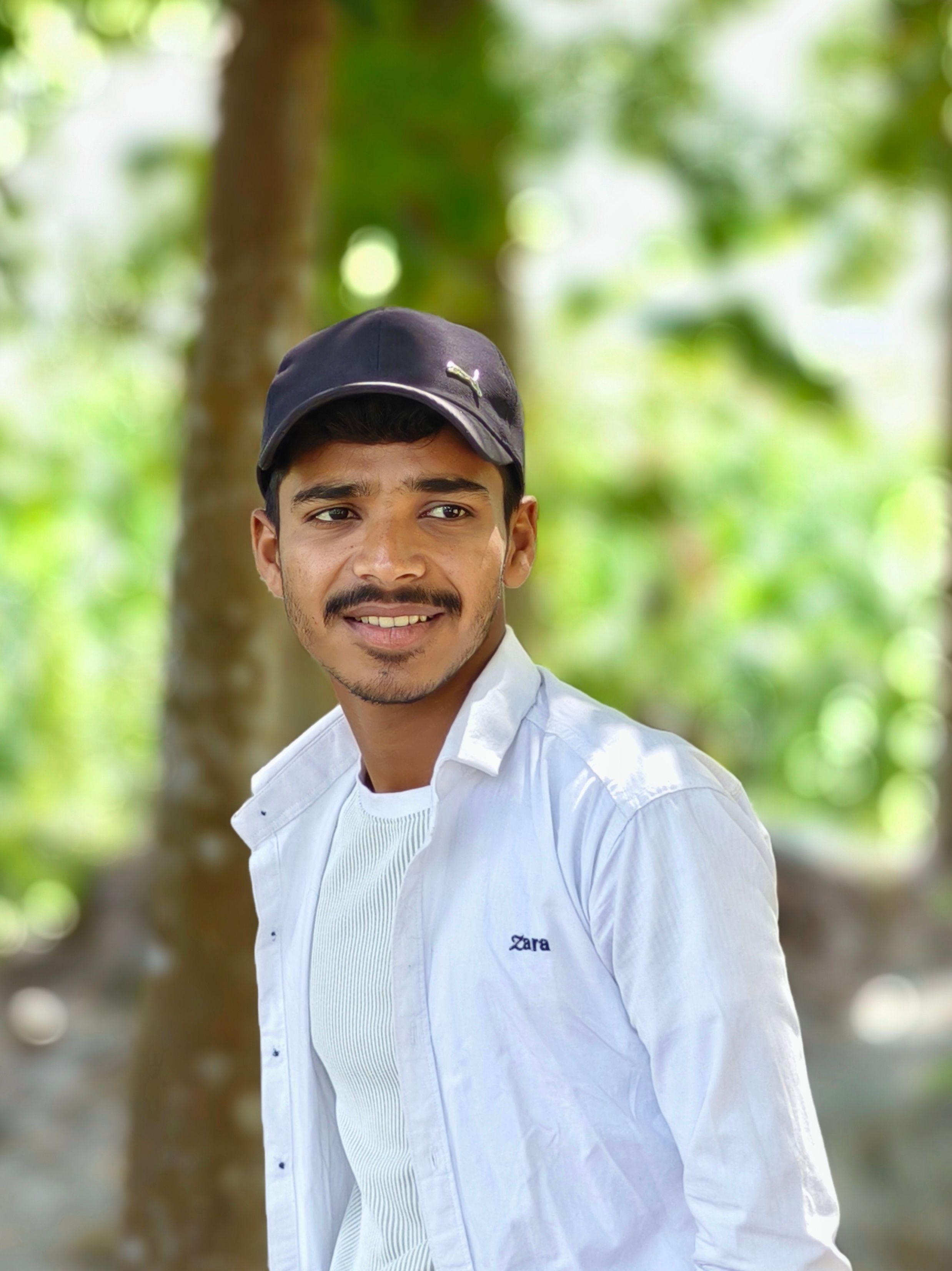 Portrait of a young man wearing a black cap and white shirt outdoors.