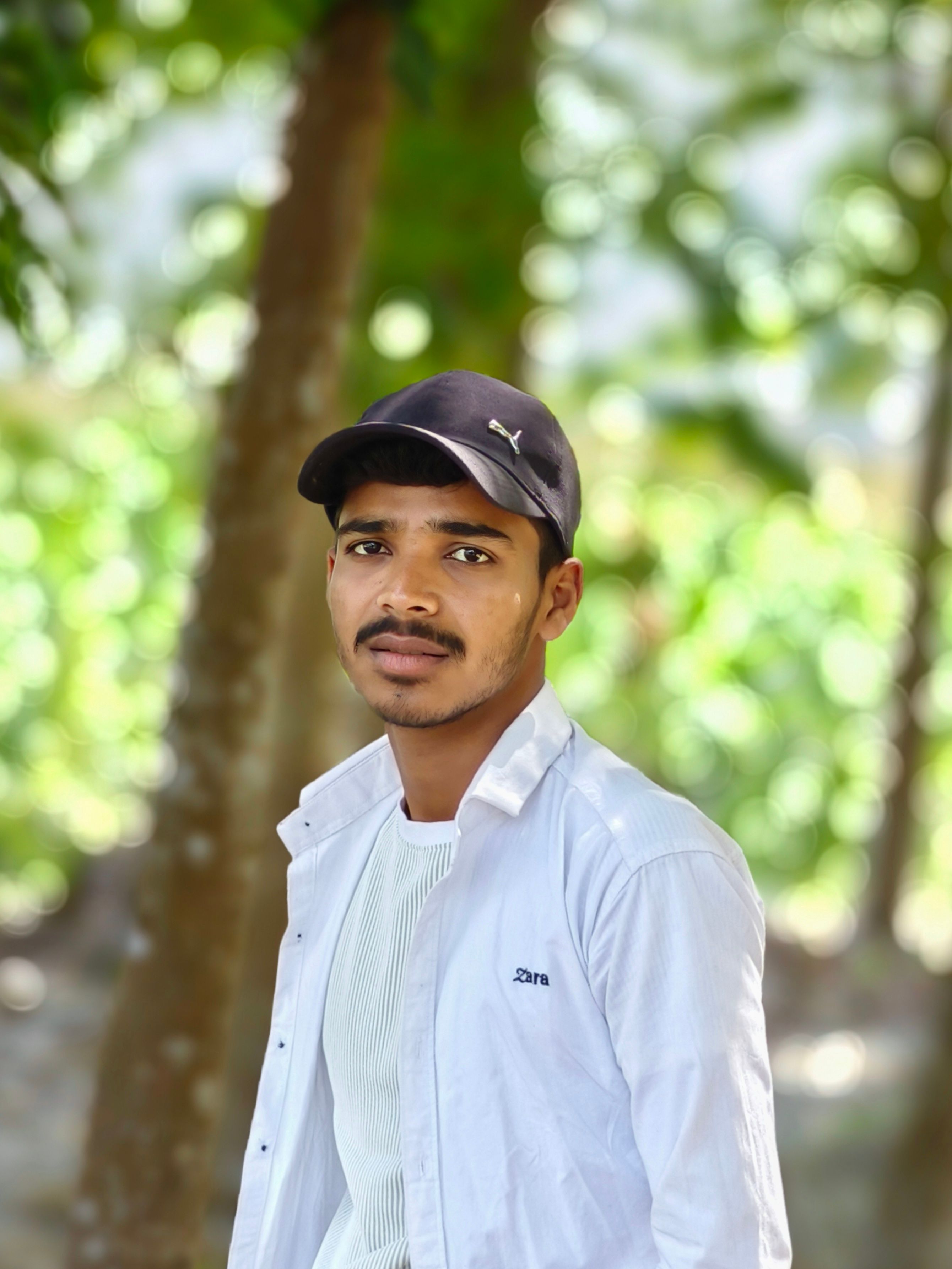 Portrait of a young man outdoors, wearing a cap and white shirt, in a natural setting.