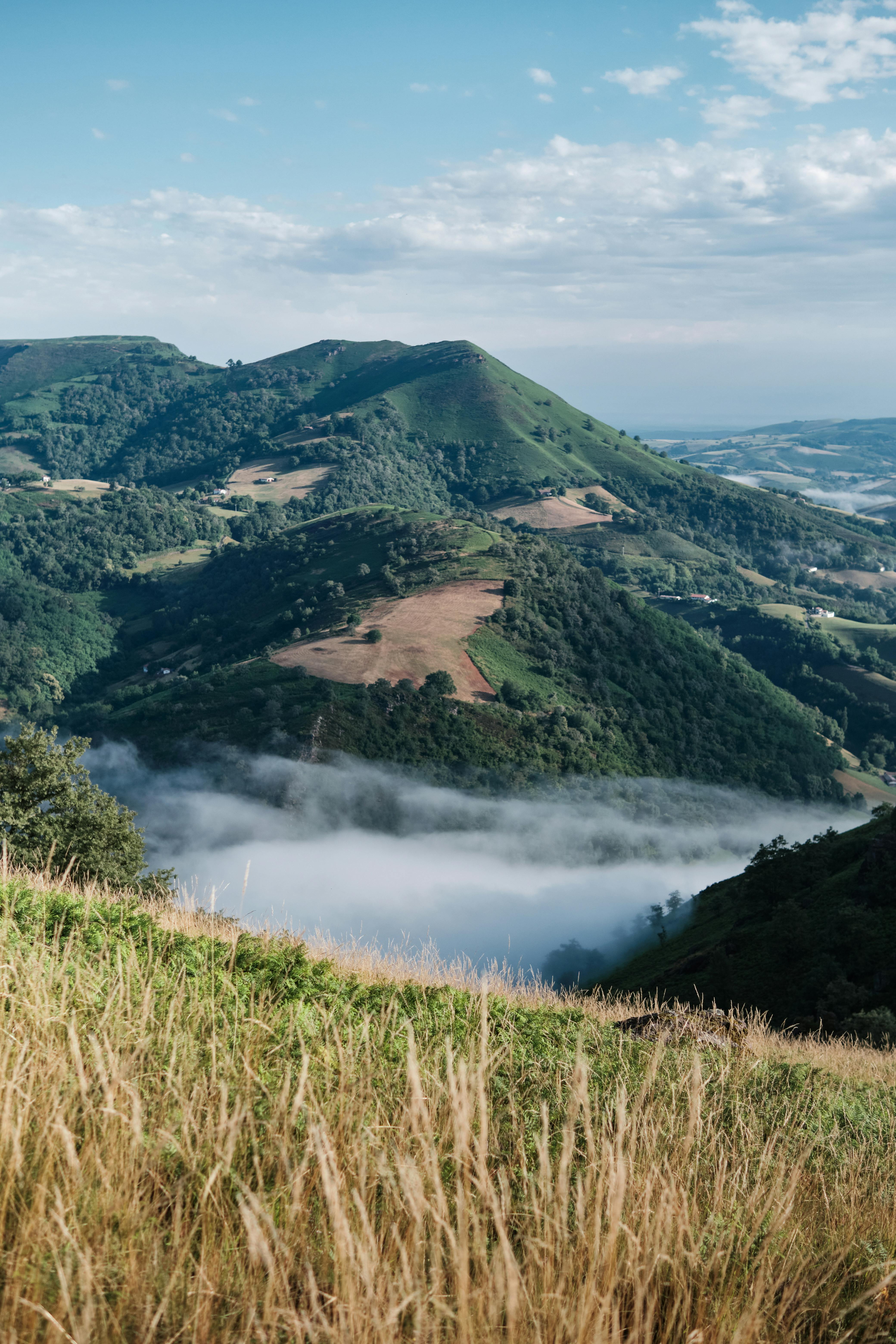 Lush green hills and misty valleys in Bidarray, France under a blue sky.