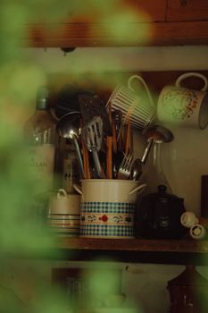 A collection of kitchen utensils and mugs on a wooden shelf, evoking a cozy, rustic feel.