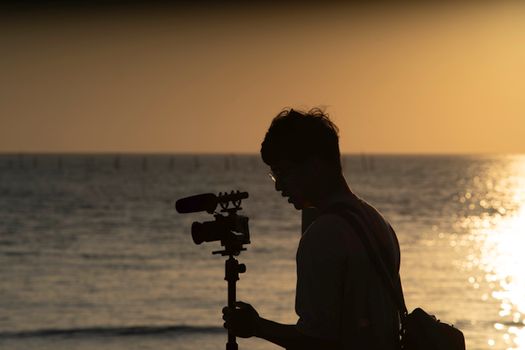 Silhouette of a videographer with a camera tripod against a stunning beach sunset in Taiwan.