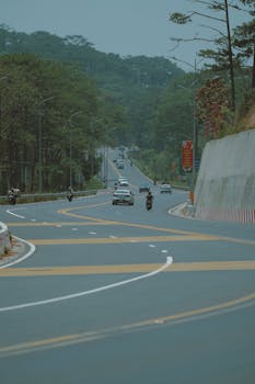 A serene highway winds through a lush forest with vehicles traveling during the day.