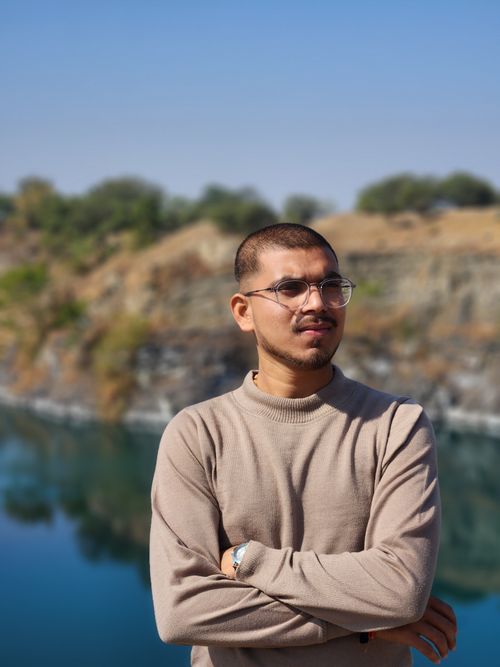 Free A man wearing glasses stands confidently by a serene lakeside, expressing tranquility. Stock Photo
