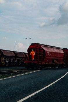 A red freight train with a worker in safety gear, showcasing industrial transportation.