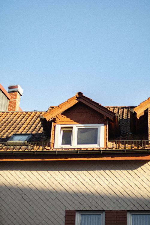 Free A quaint European building roof highlighted by a dormer window under a clear blue sky. Stock Photo