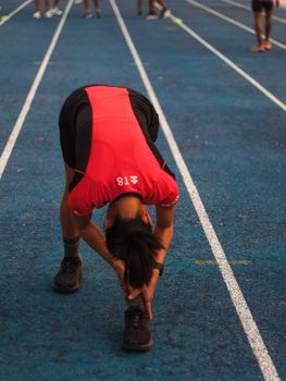 Athlete in red jersey stretches on blue track before race, preparing for action.