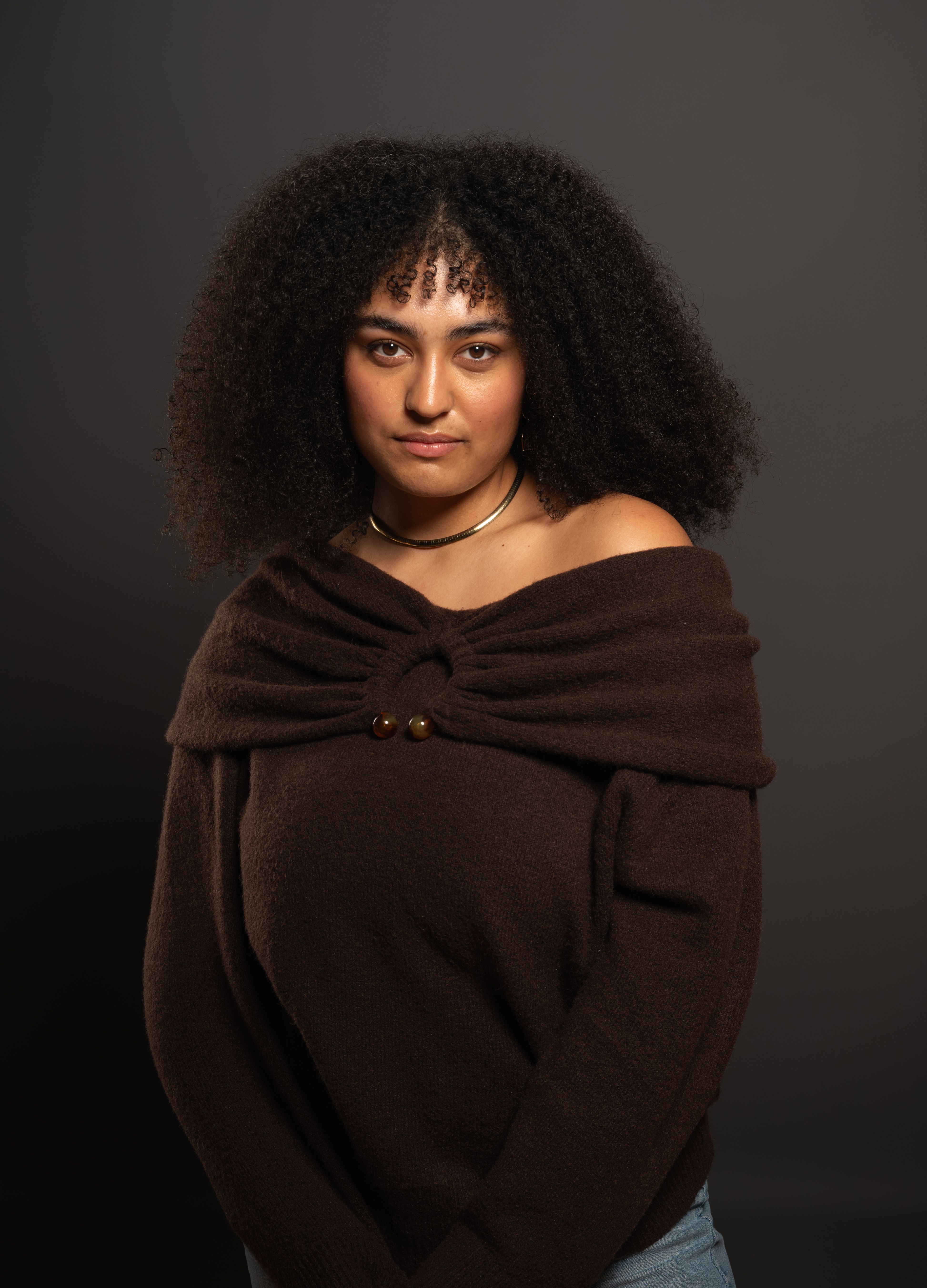 Portrait of a young woman wearing a brown sweater against a neutral background, conveying warmth and confidence.