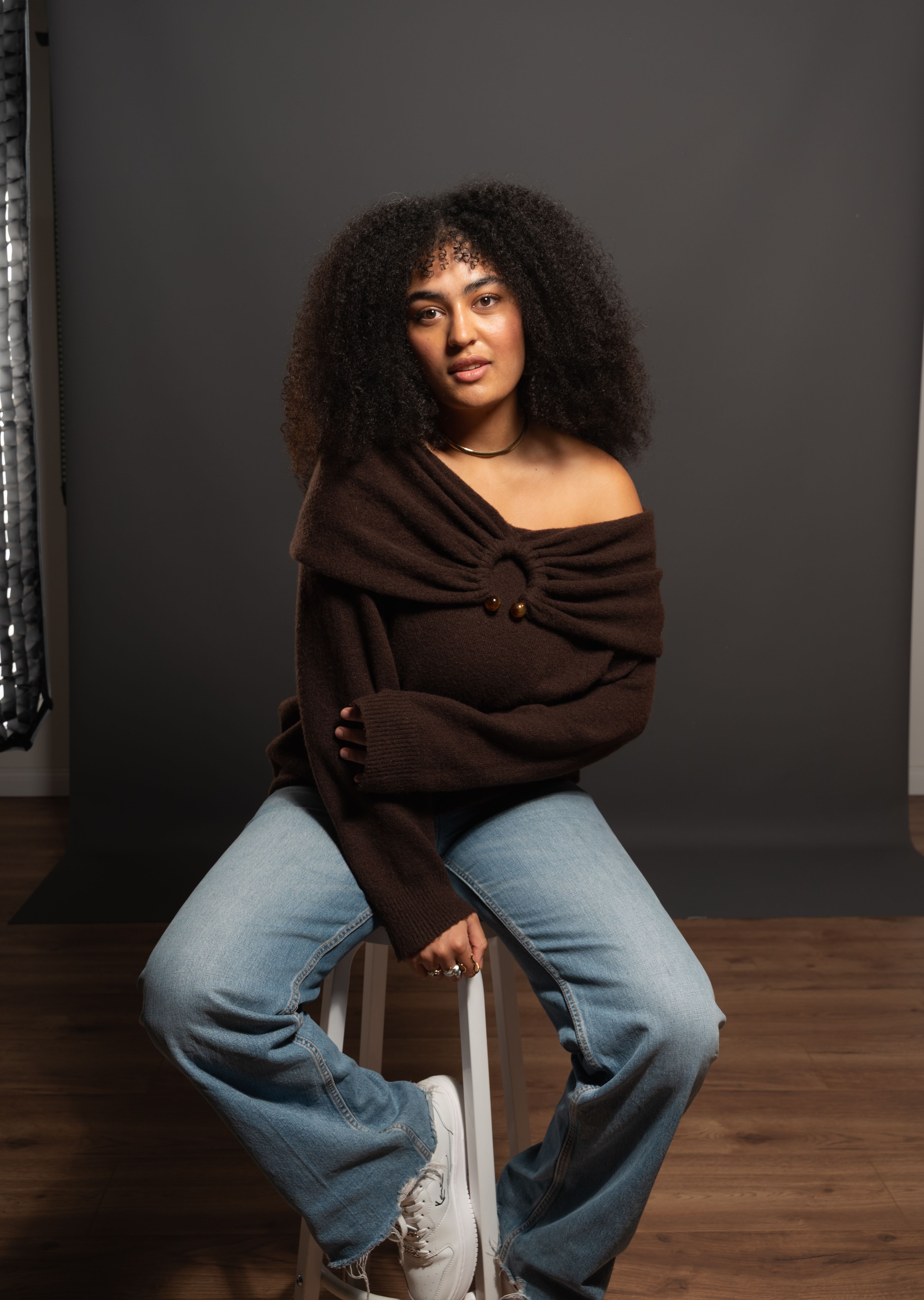 Young woman with curly hair posing in a studio setting, showcasing contemporary fashion.