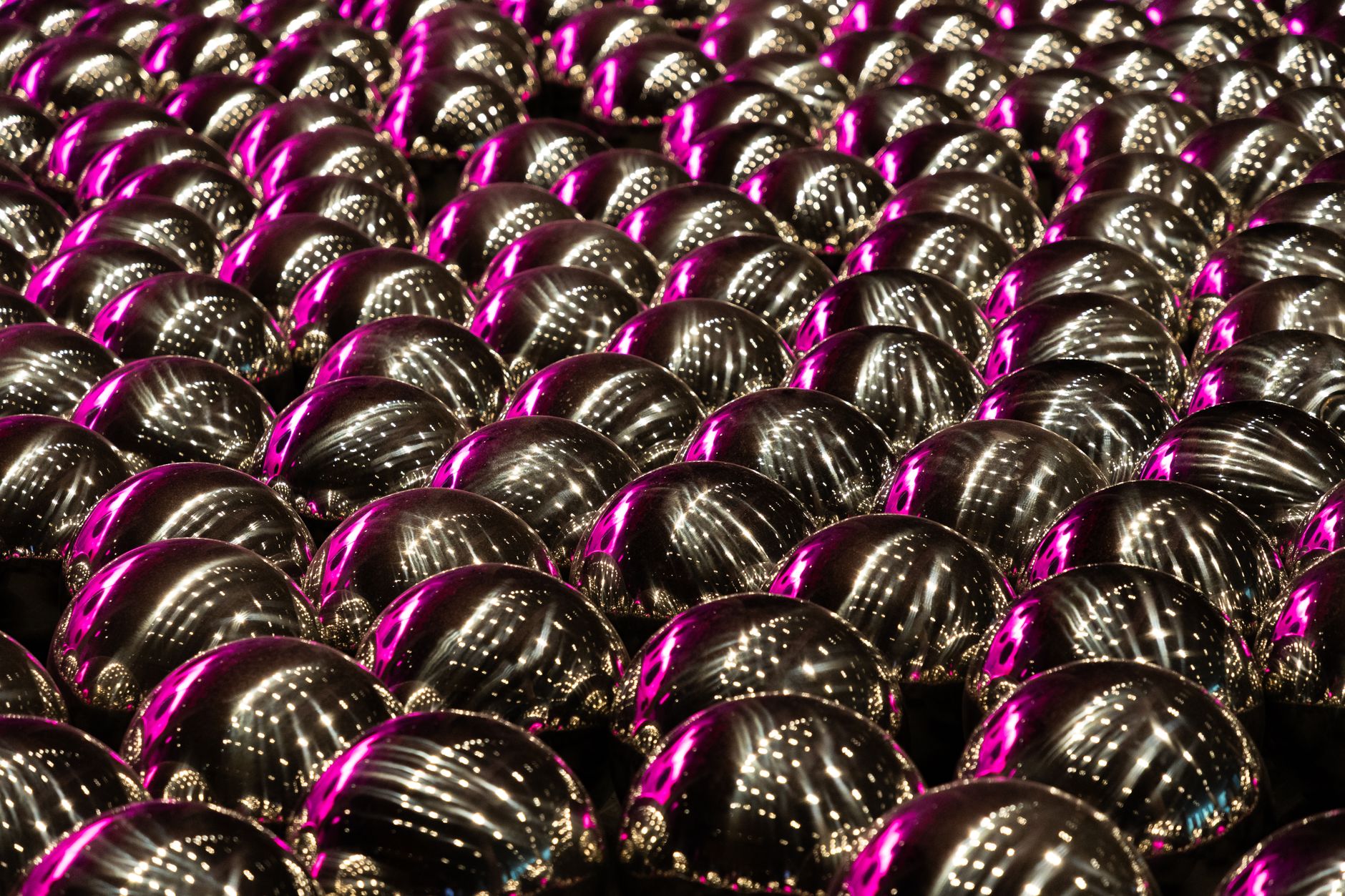 Array of metallic spheres reflecting pink lights, creating an abstract pattern.