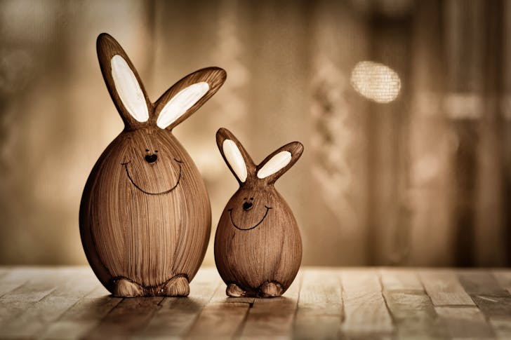 Wooden eggs in form of rabbits with big ears and lines with dots representing muzzle placed on table in room with artificial light during Easter holiday