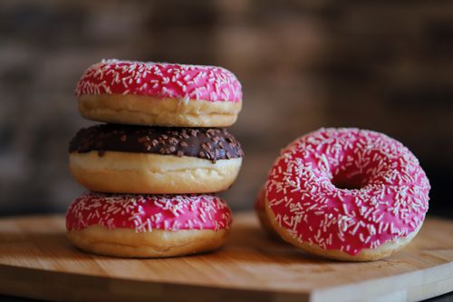Free Close-up of vibrant pink and chocolate frosted doughnuts with sprinkles stacked on a wooden board. Stock Photo