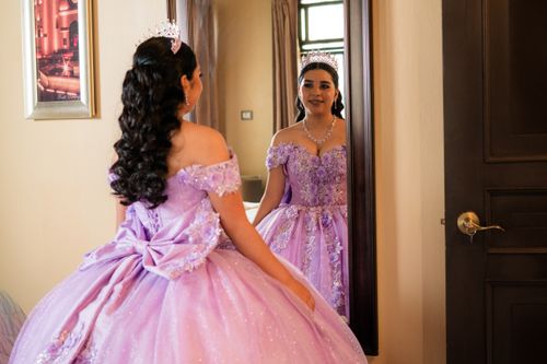 Free Elegant young woman in a lavender gown and tiara admiring her reflection in an ornate indoor setting. Stock Photo