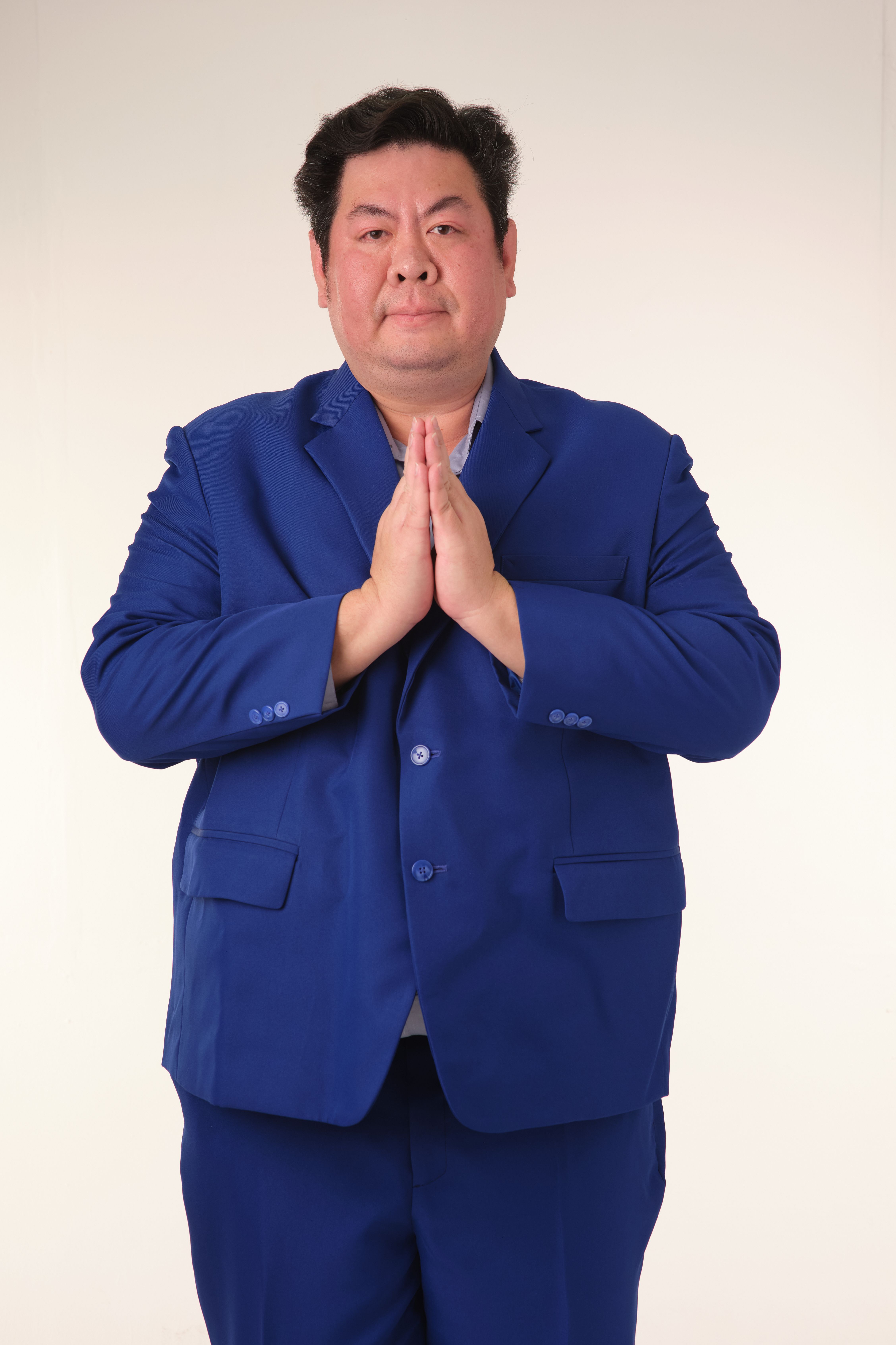 Portrait of a businessman in a blue suit with hands in a prayer pose against a neutral background.