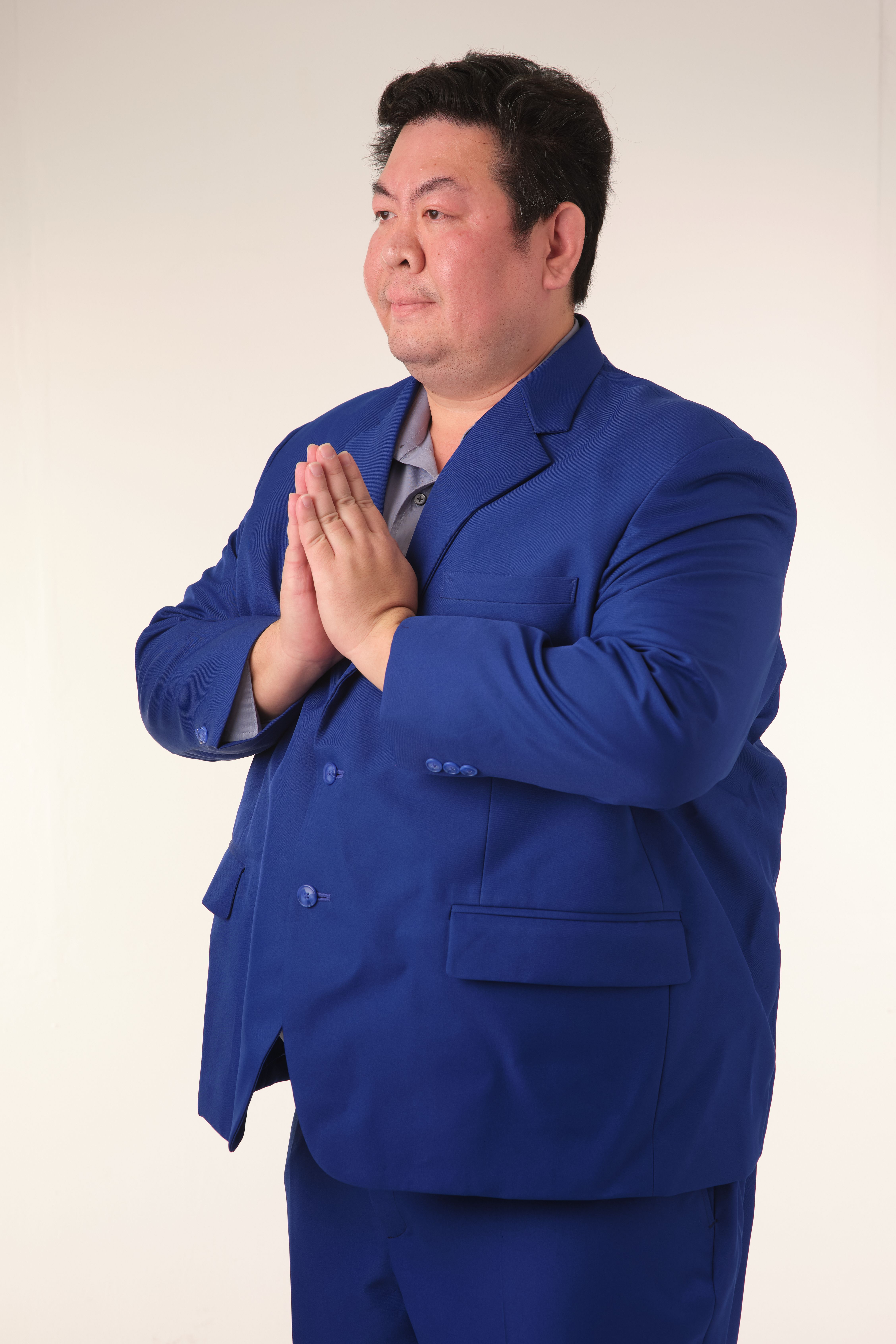 An adult man in a blue suit practicing meditation indoors with hands in prayer position.