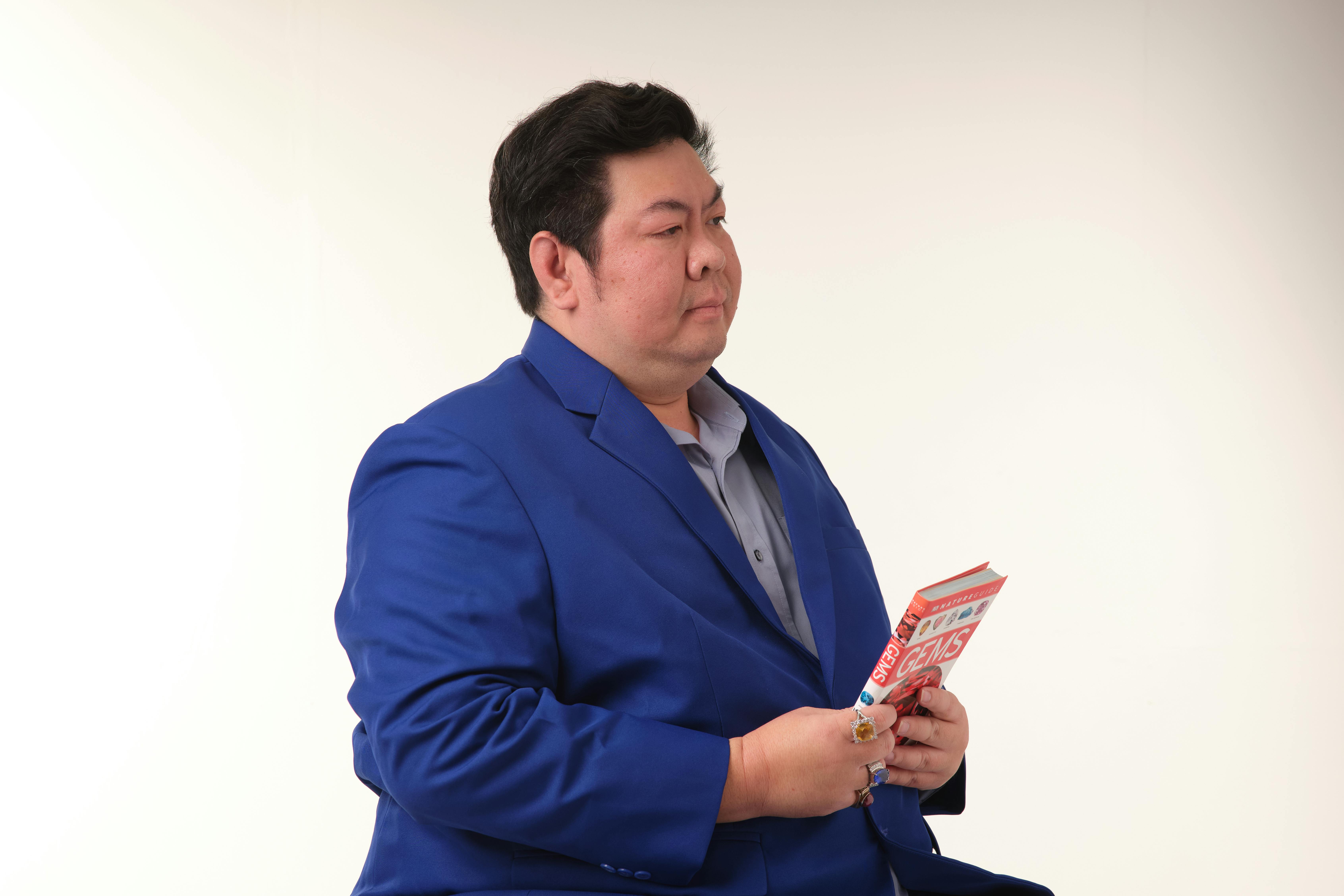 Gratuit Bărbat într-un costum albastru care ține o revistă pe un fundal simplu. Fotografie de stoc