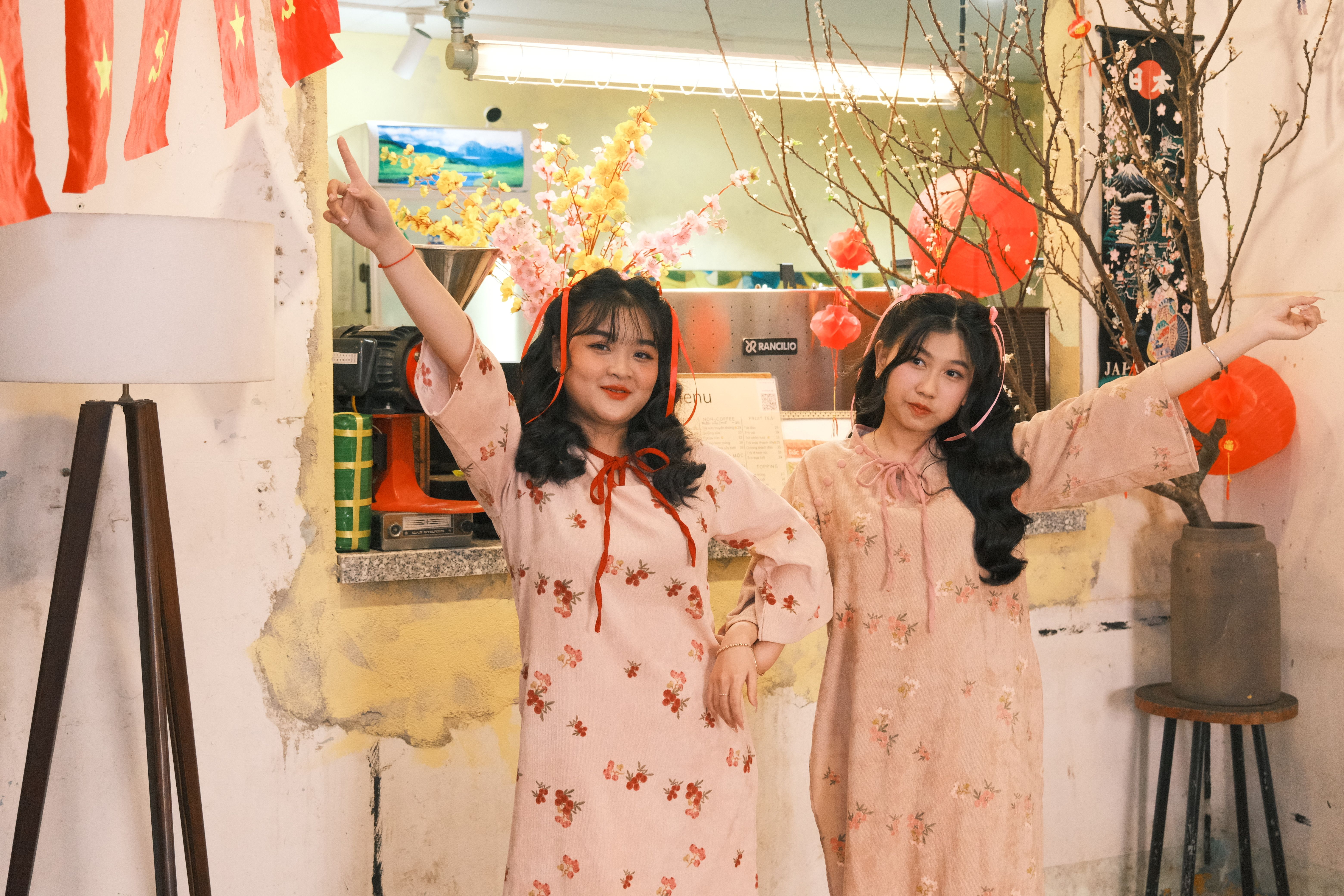 Two Asian women in floral dresses celebrating Lunar New Year indoors with festive decorations.