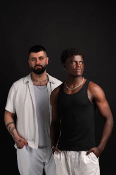 Portrait of two men of different ethnicities posing together in a studio setting with a dark background.