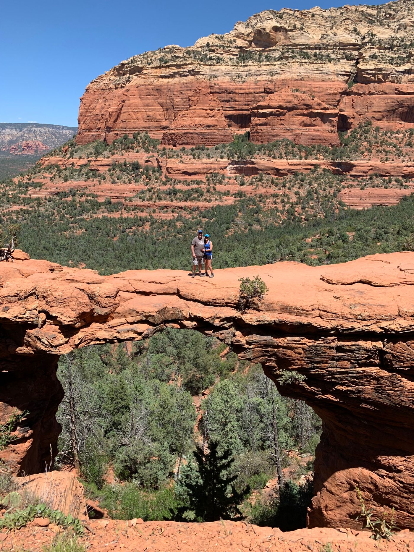 Hikers standing on Devil’s Bridge above Sedona’s red rock landscape